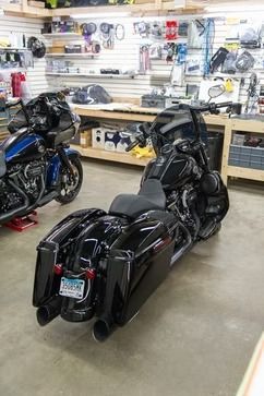 Black touring motorcycle with saddlebags in a garage, beside a blue motorcycle and workshop tools.