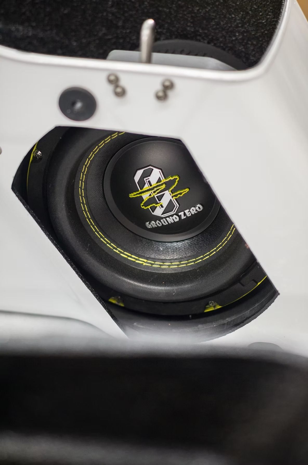 Close-up of a black speaker driver mounted in a white enclosure, with yellow stitching detail.