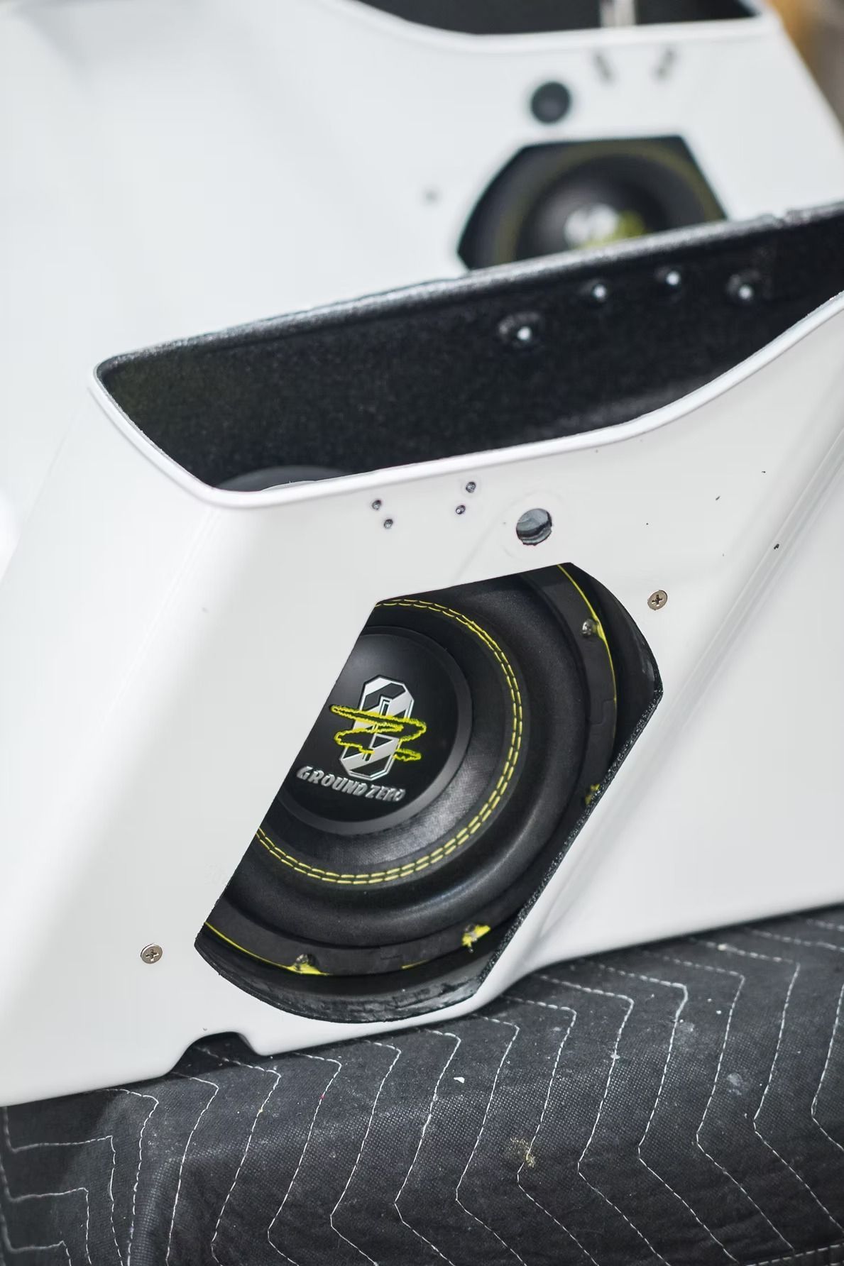 Close-up of a white car body panel with a black speaker and visible mounting hardware