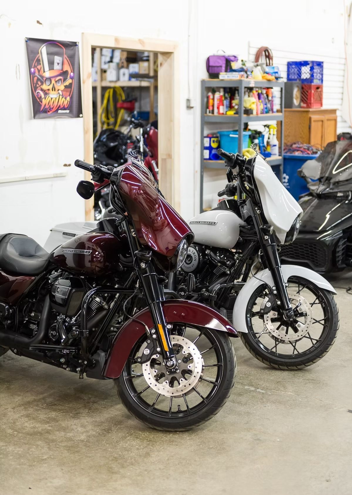 Two motorcycles parked in a garage, one maroon and one white, with shelves and tools in the background