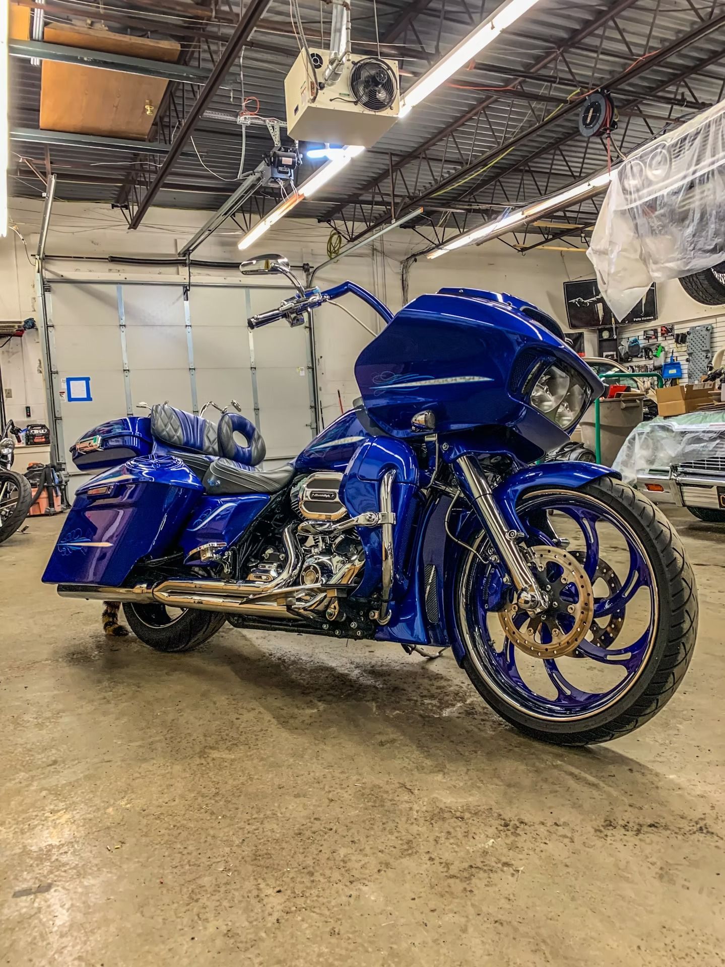 Blue custom touring motorcycle with sidecar in a workshop garage, chrome details and large front wheel.