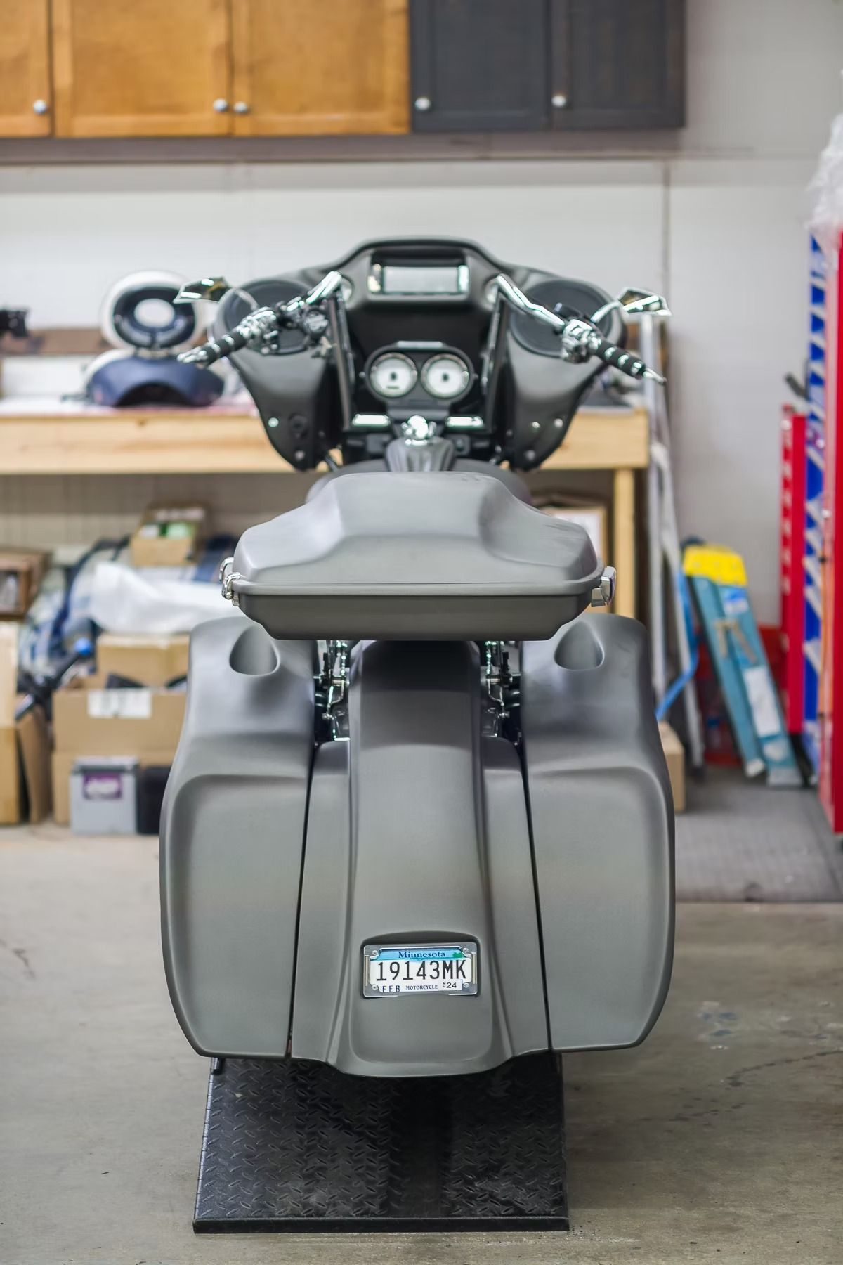 Gray scooter parked in a garage, front view with handlebars and large storage compartments.