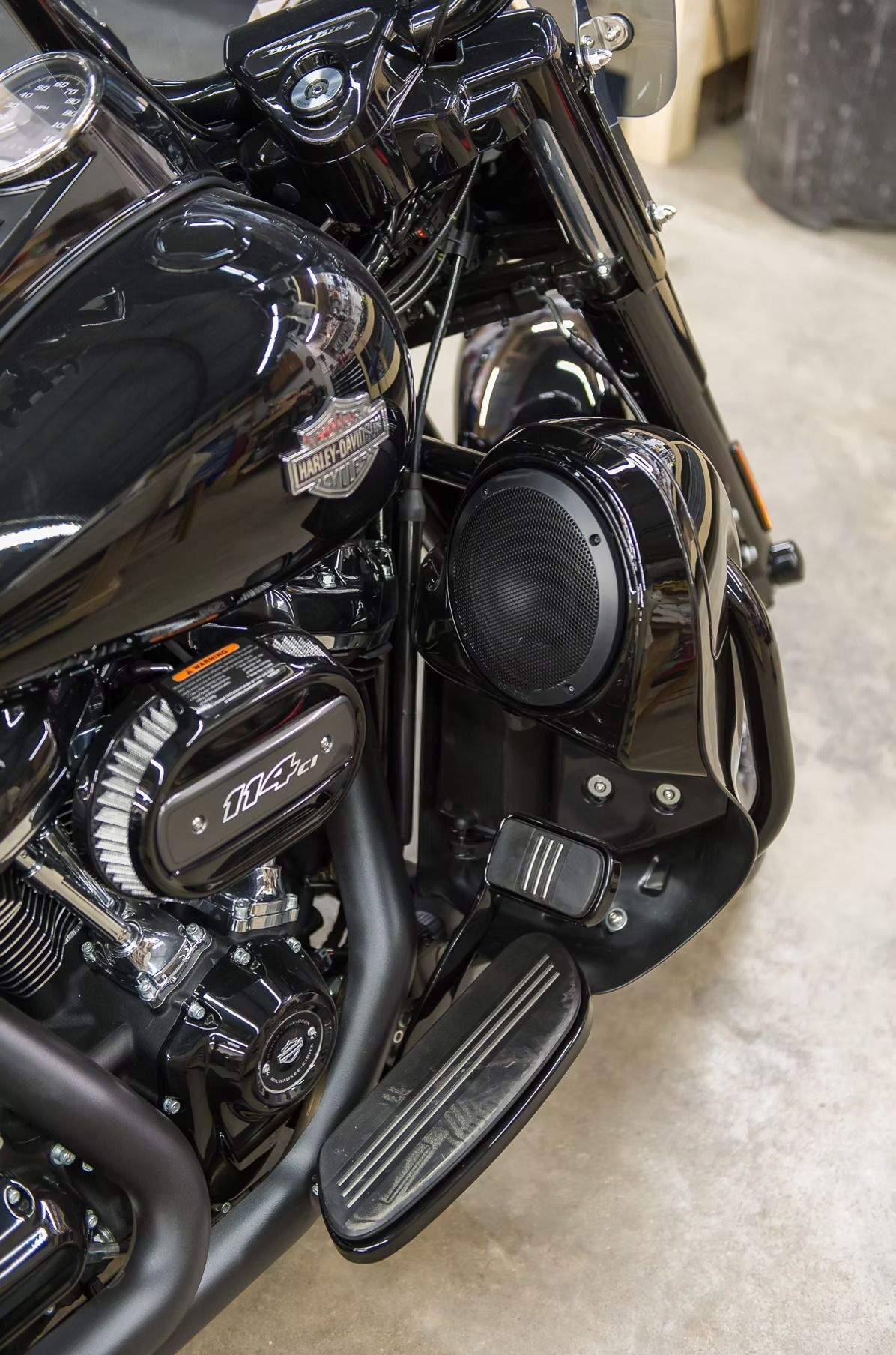 Black motorcycle close-up with chrome engine, round speaker, and footboard in a garage