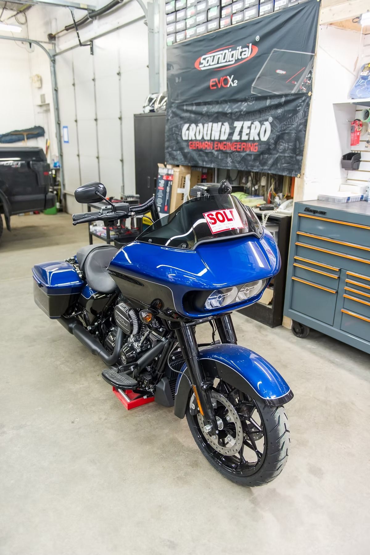 Blue touring motorcycle in a garage workshop, with black accents and tool cabinets in the background