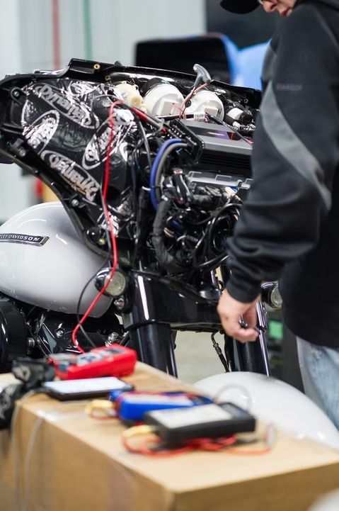 Person working on a motorcycle engine with exposed wires and tools in a garage area