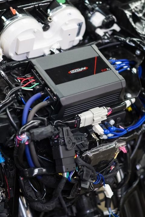 Car engine bay with black ECU control box and visible wiring, hoses, and white fluid reservoirs