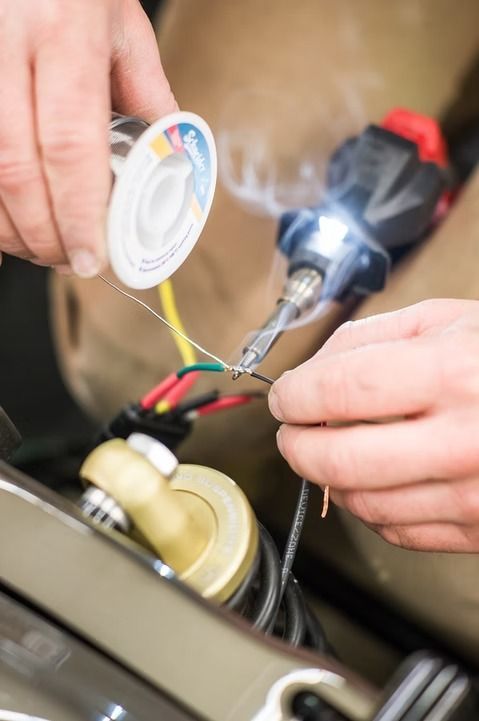 Hands soldering wires to an electronic component with a heated soldering iron in a workshop area