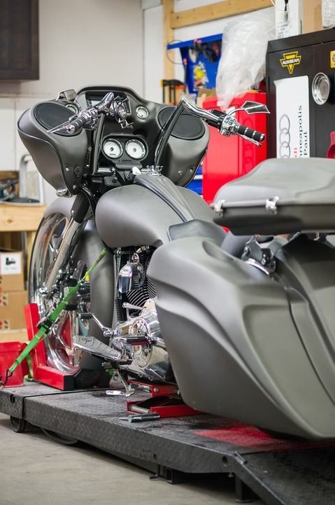 Black touring motorcycle on a workshop lift with a red lift strap and gray seat backrest