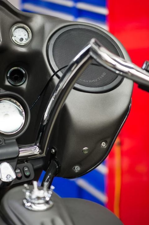 Close-up of a black motorcycle speaker and chrome handlebar against a red and blue background