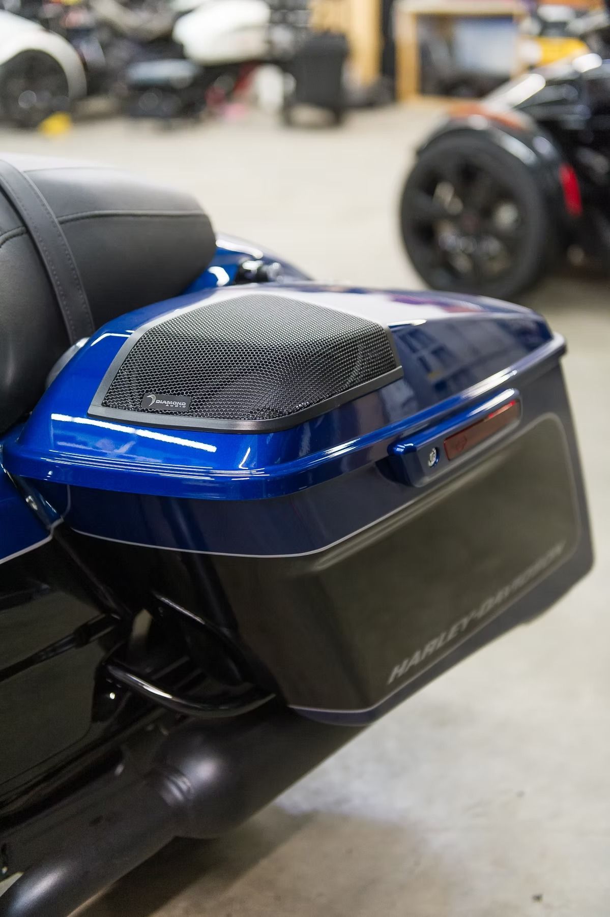 Blue motorcycle luggage box with black side case and mesh vent in a workshop.