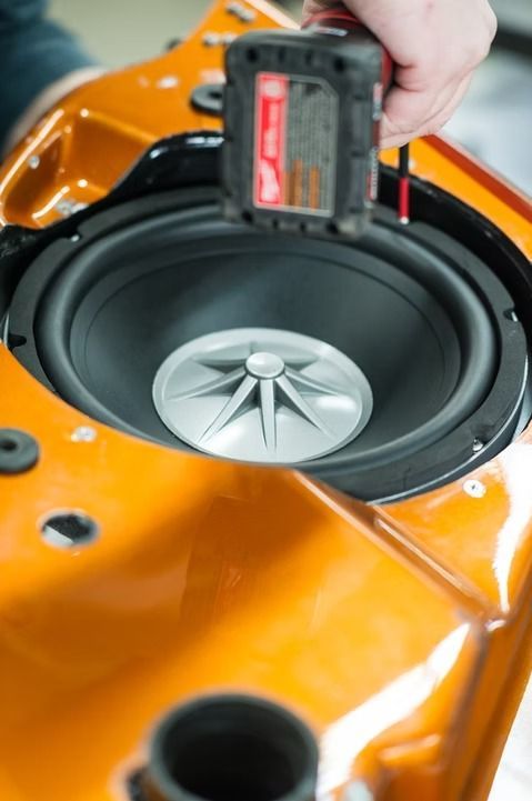 Hand measuring a black speaker in an orange car door panel during installation