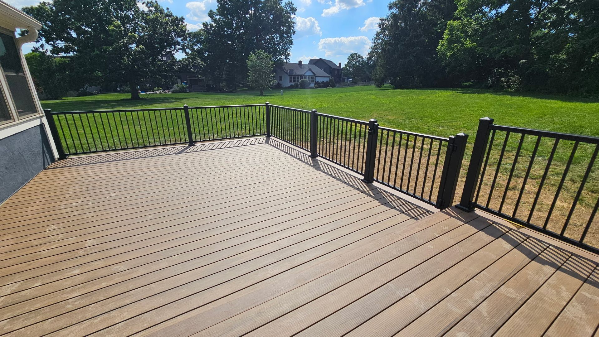A wooden deck with a metal railing and a grassy field in the background.