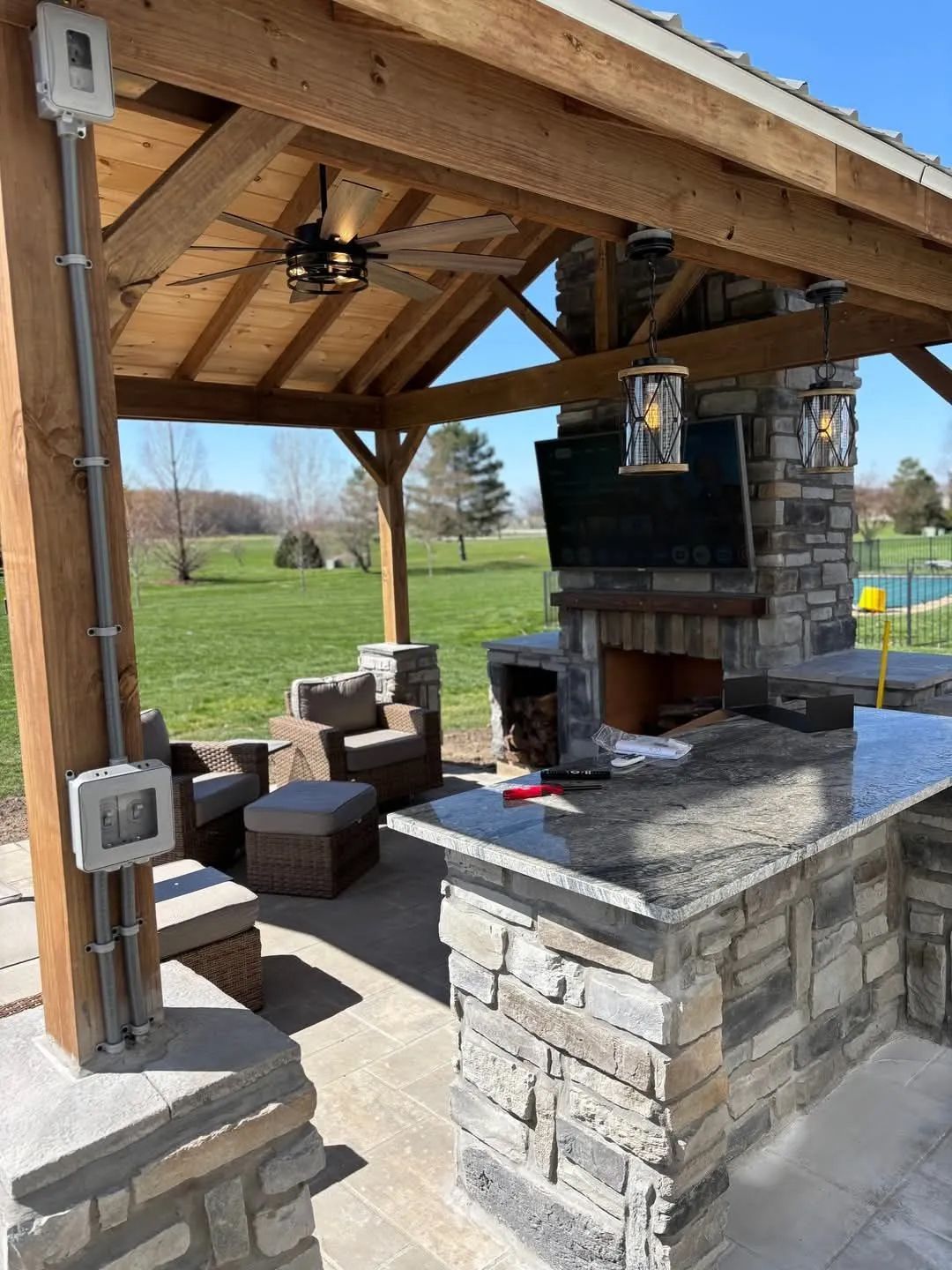 A patio with a ceiling fan, a television, a fireplace, a table and chairs.