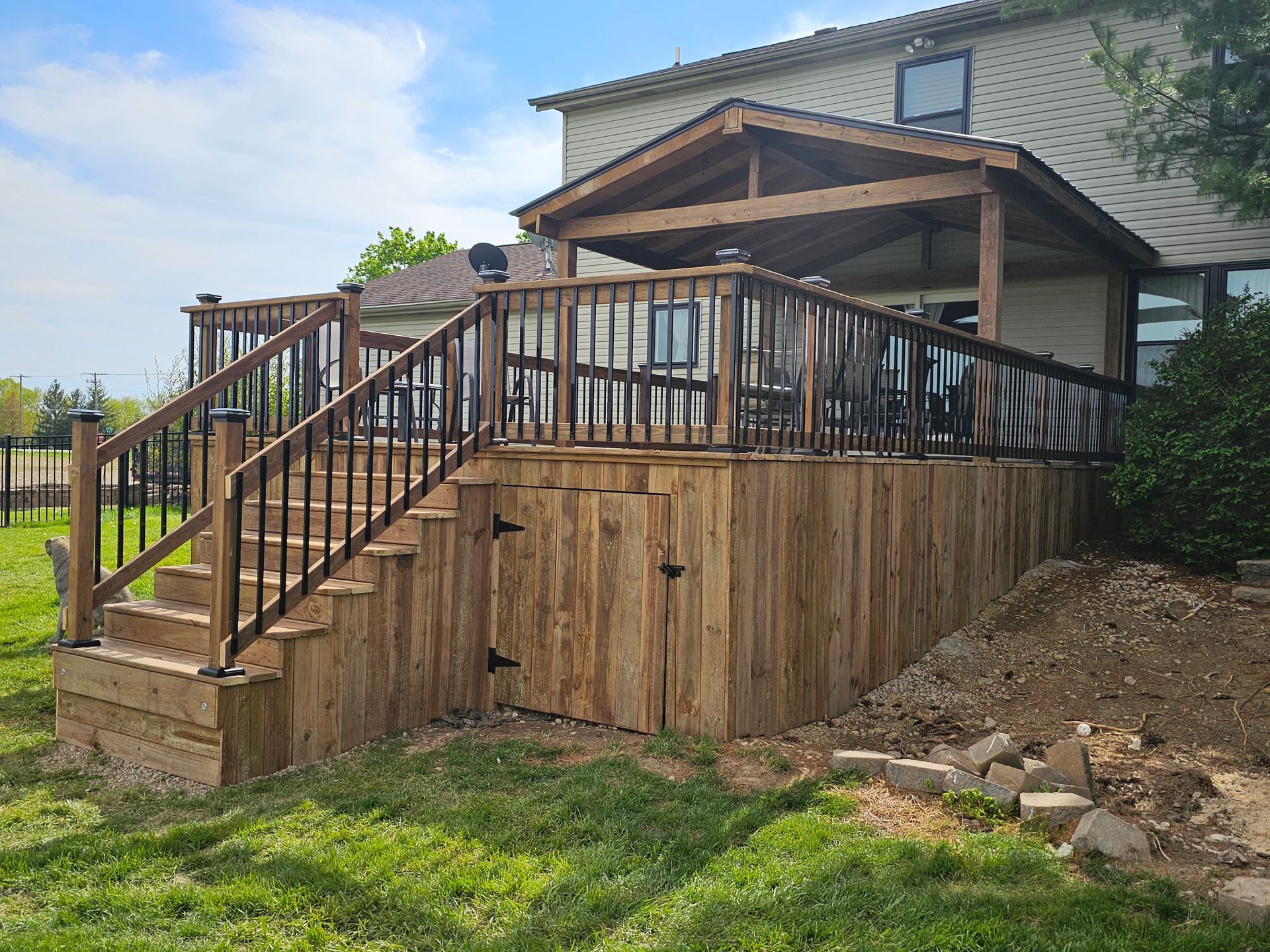 A wooden deck with stairs leading up to it is in the backyard of a house.
