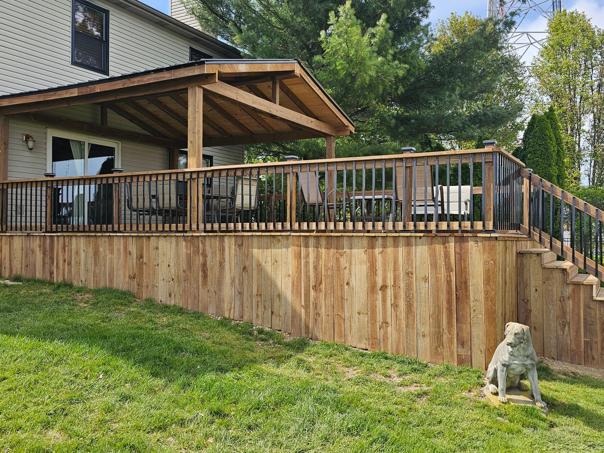 A wooden deck with a covered patio and stairs is sitting on top of a lush green hillside.