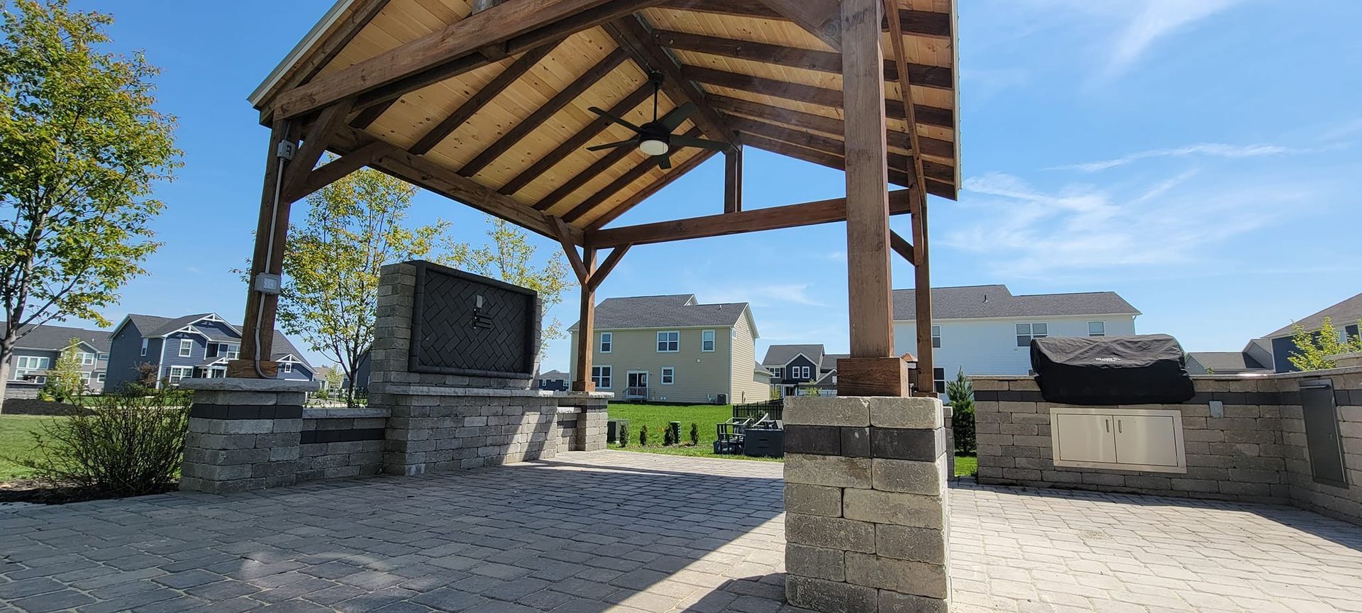 A wooden gazebo with a grill underneath it in a park.