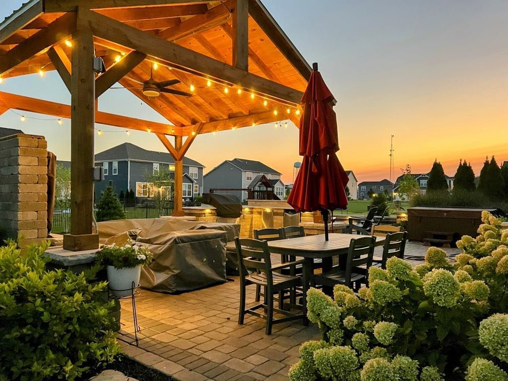 A patio with tables and chairs under a wooden gazebo at sunset.