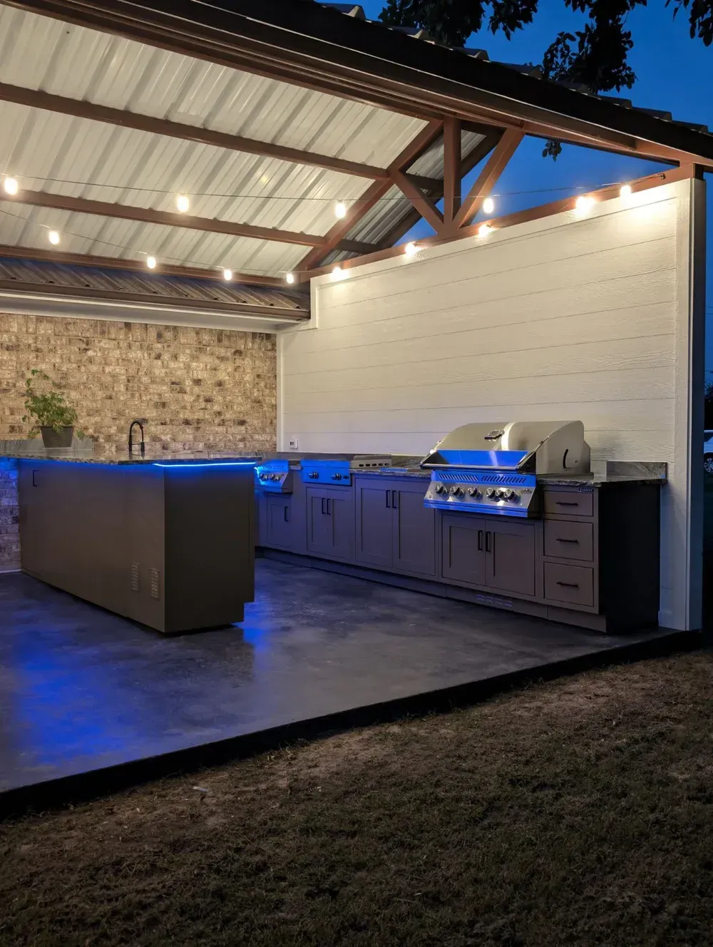 A large outdoor kitchen with a grill and cabinets at night