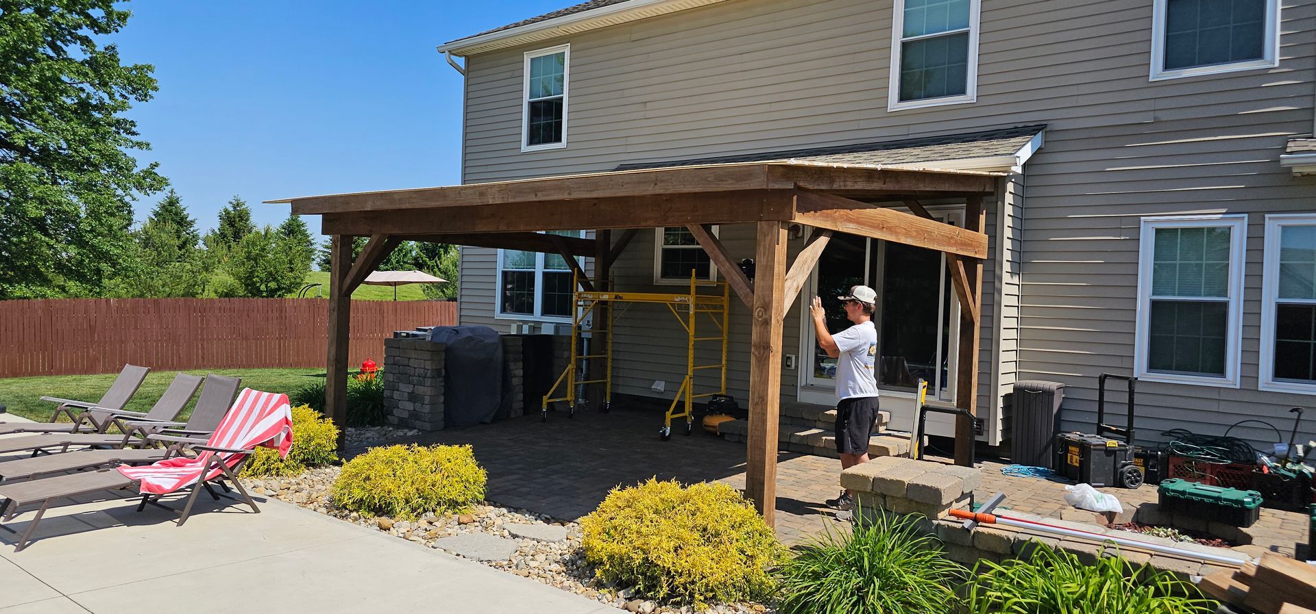 A man is working on a wooden pergola in front of a house.