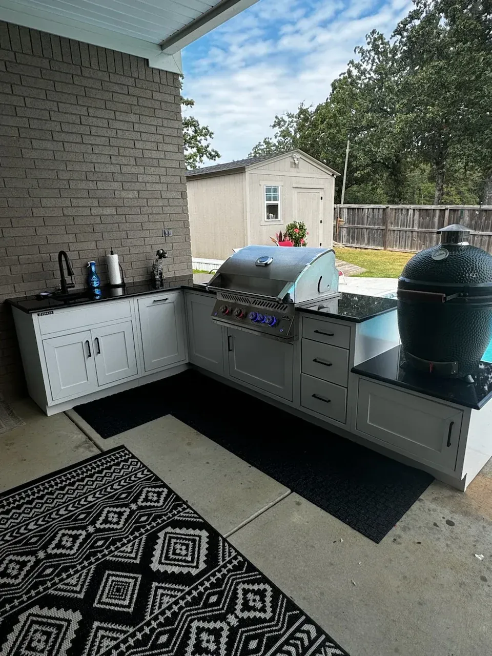 An outdoor kitchen with a grill , sink , and rug.