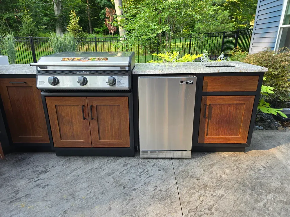 An outdoor kitchen with a grill and a refrigerator.