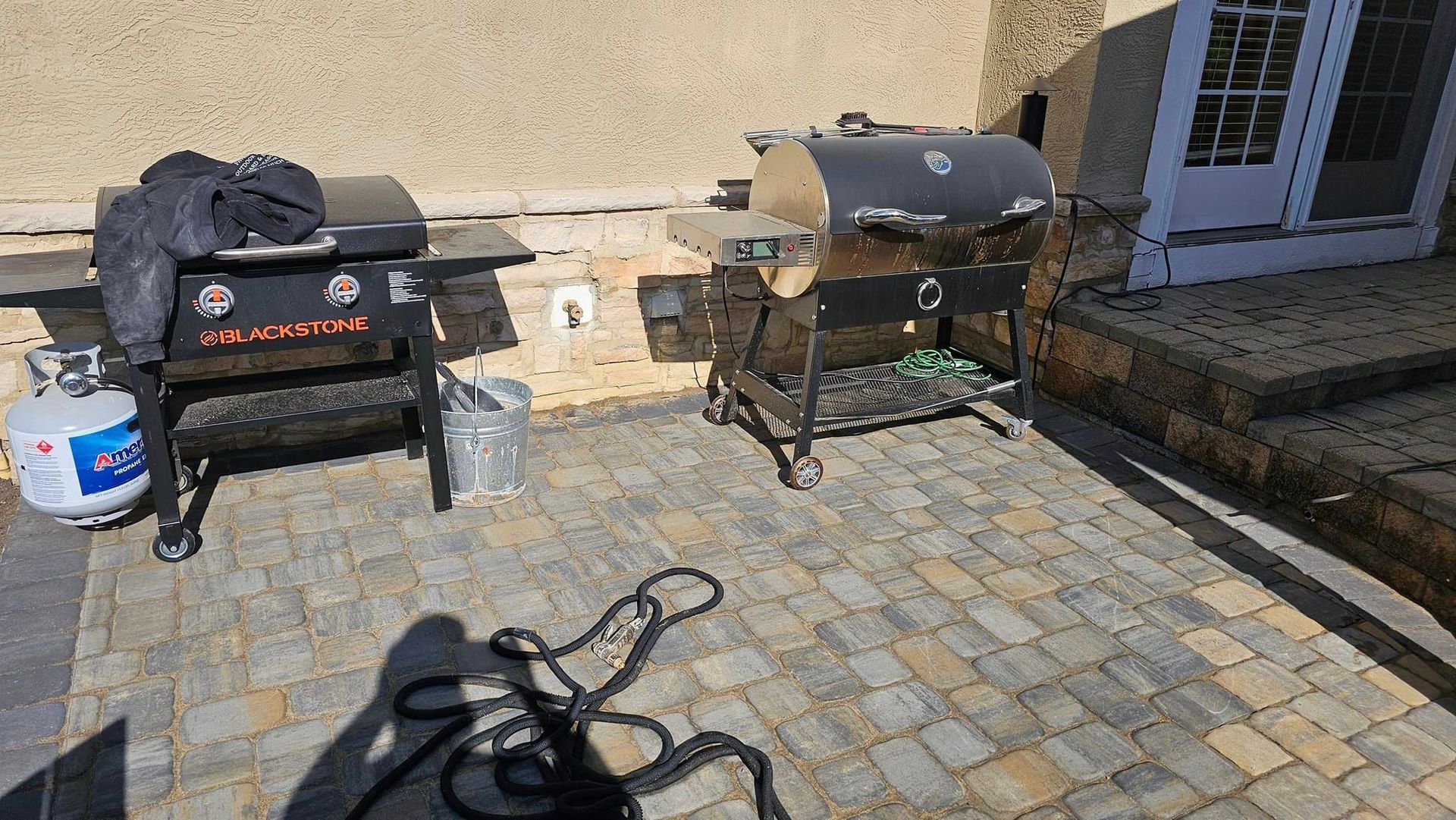 Two grills are sitting on a patio next to a propane tank.