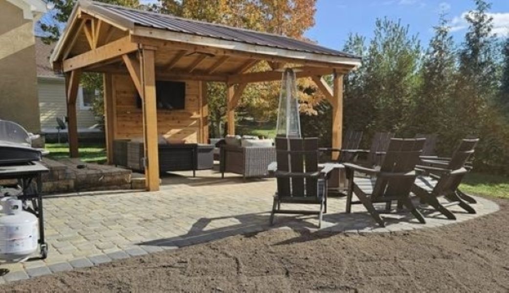 A wooden gazebo with chairs and a grill in a backyard.