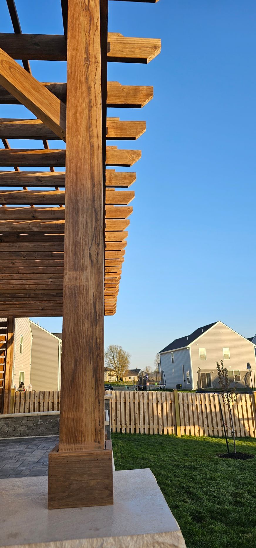 A wooden pergola is sitting in the middle of a lush green yard.