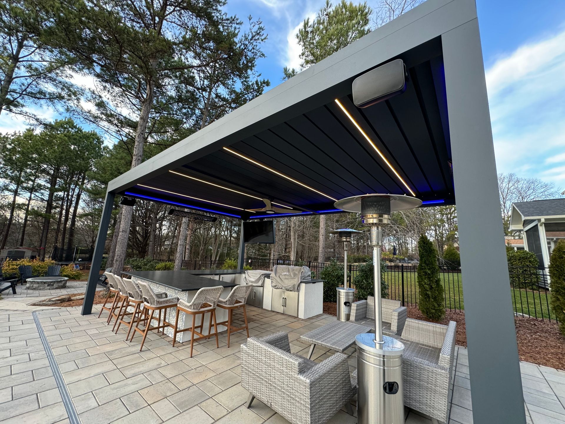 A patio with a pergola, chairs, tables and a grill.