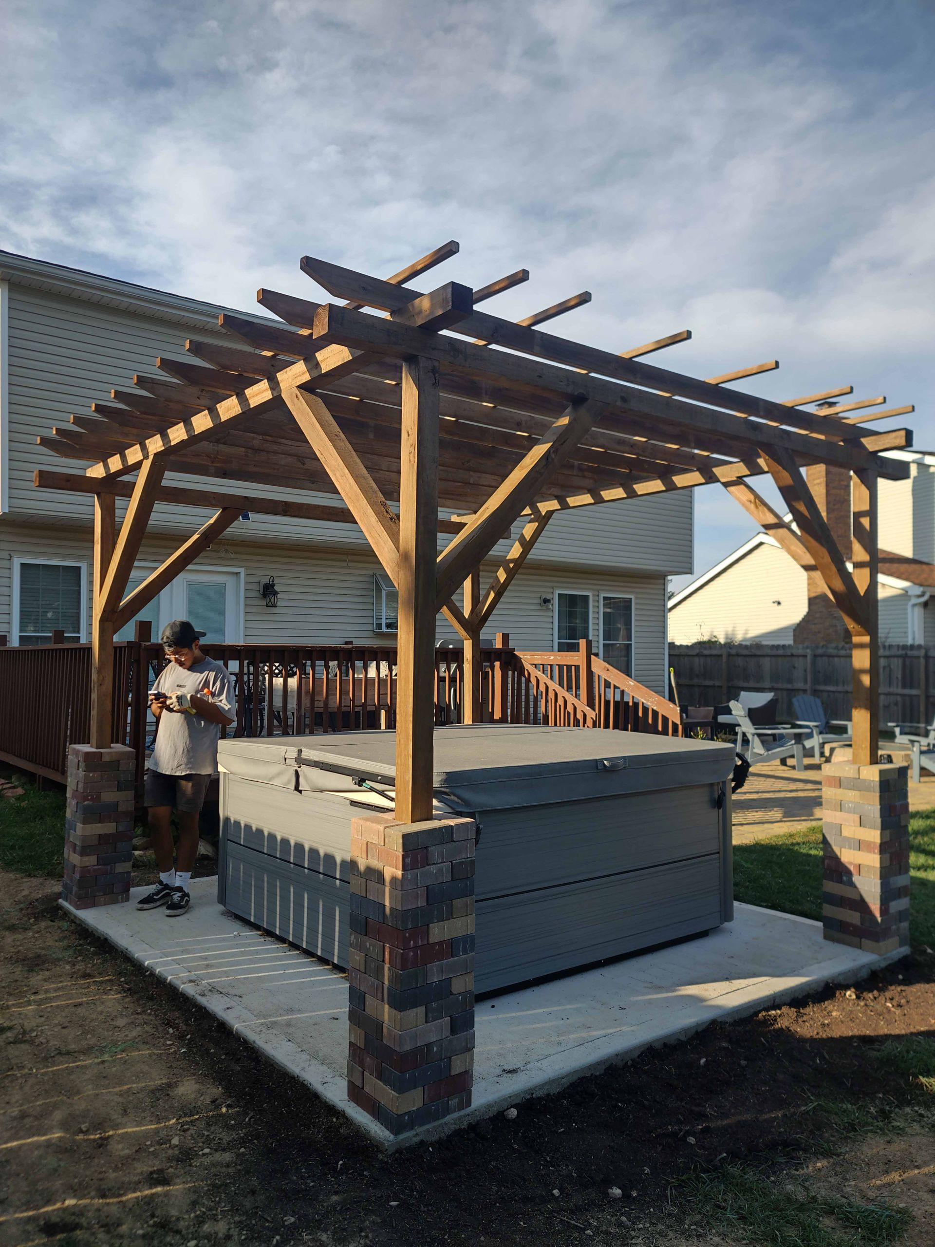 A man is standing under a pergola next to a hot tub.