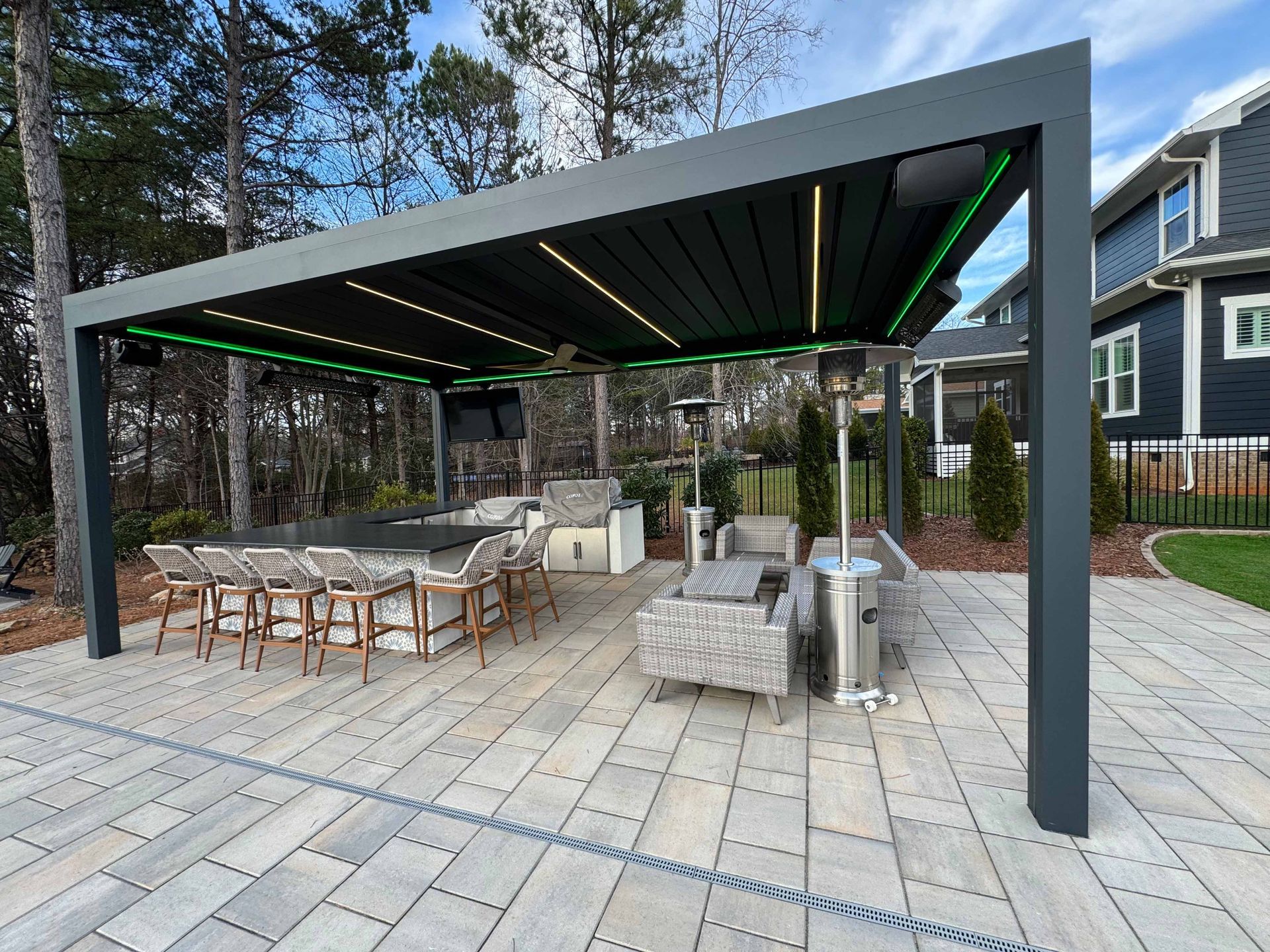 A patio with a pergola , tables , chairs , and a kitchen.