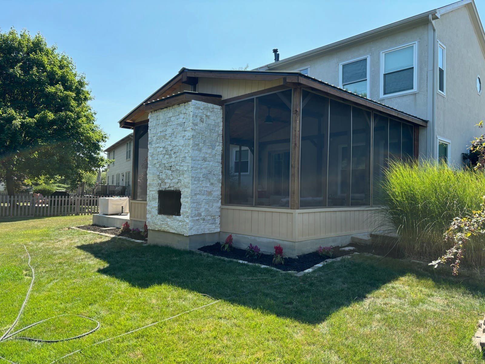 A screened in porch with a fireplace in the backyard of a house.