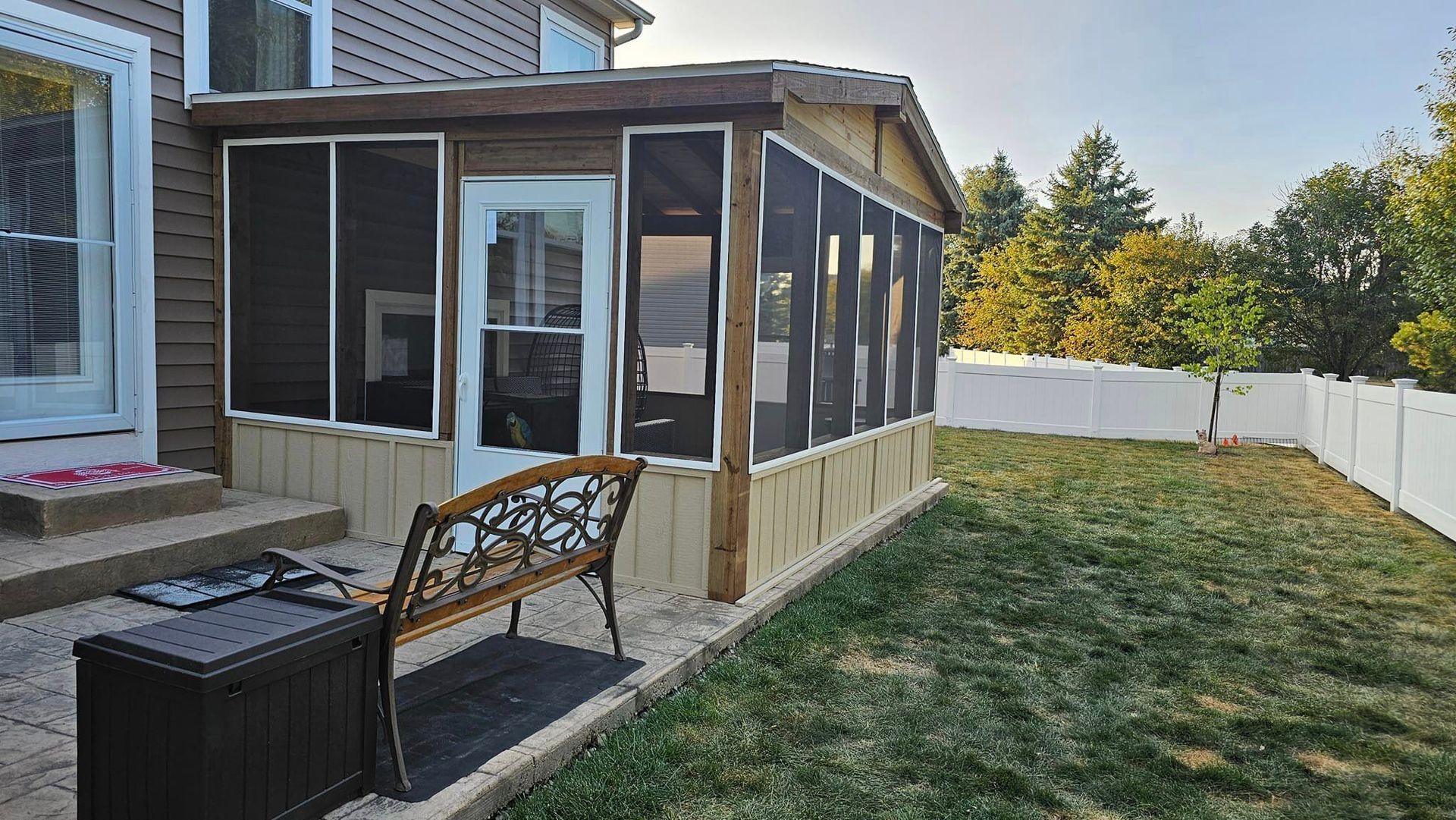 A screened in porch with a bench in the backyard of a house.