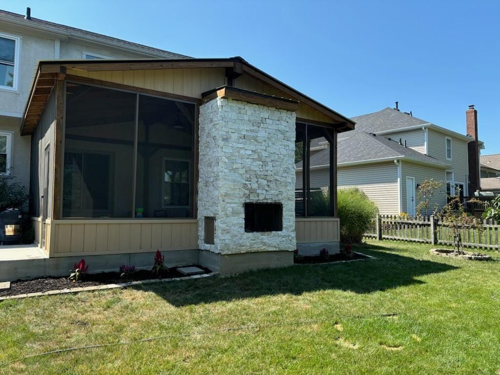 A screened in porch with a fireplace in the backyard of a house.