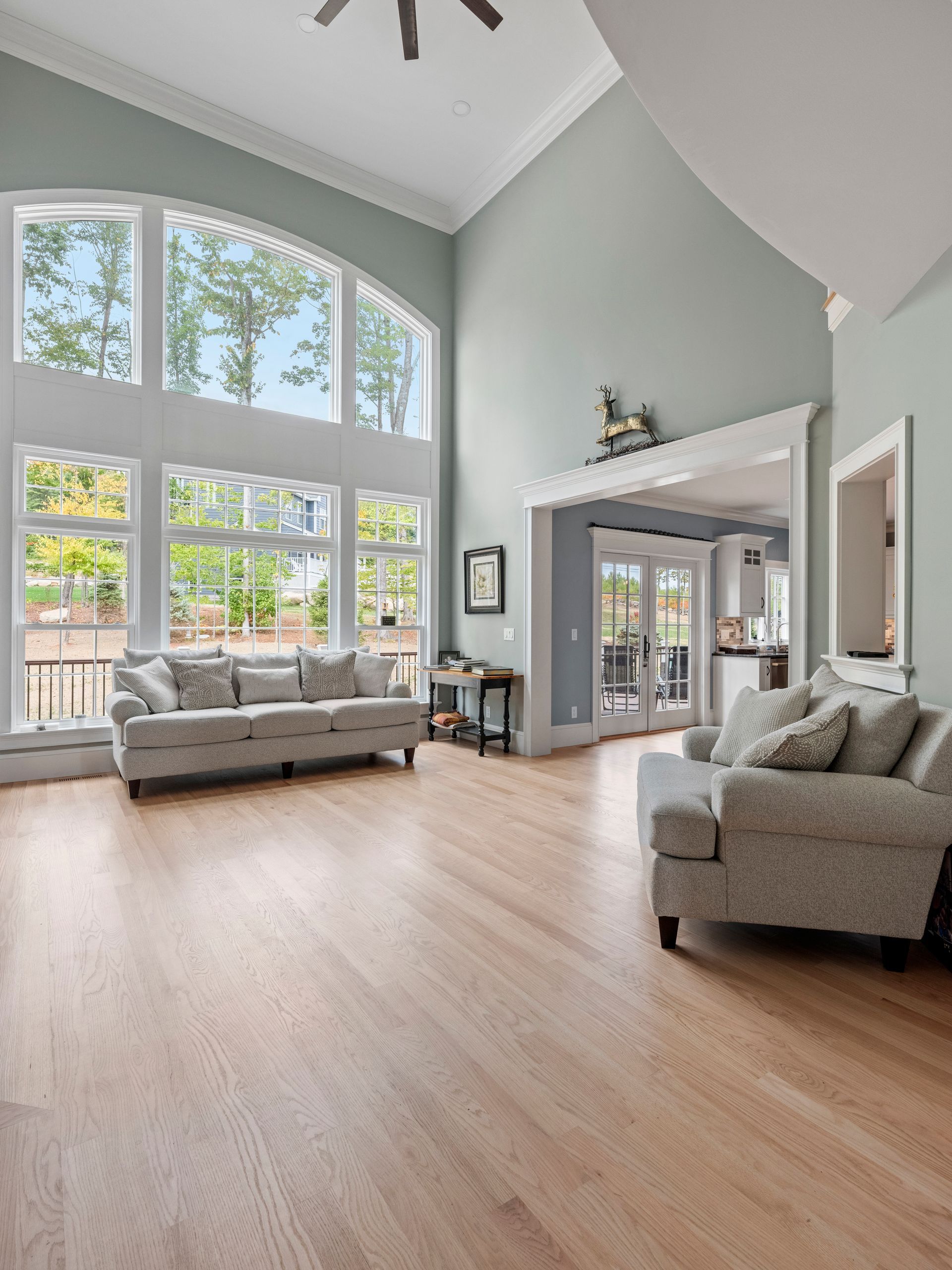 Spacious living room with hardwood floors, large windows, two couches, and a view of trees.