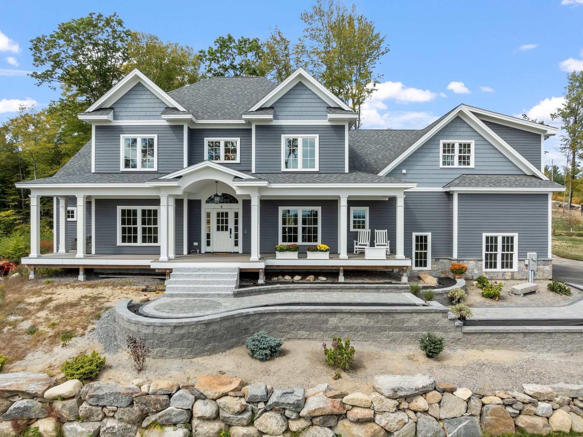 Gray two-story house with white trim, a front porch, and stone retaining wall.