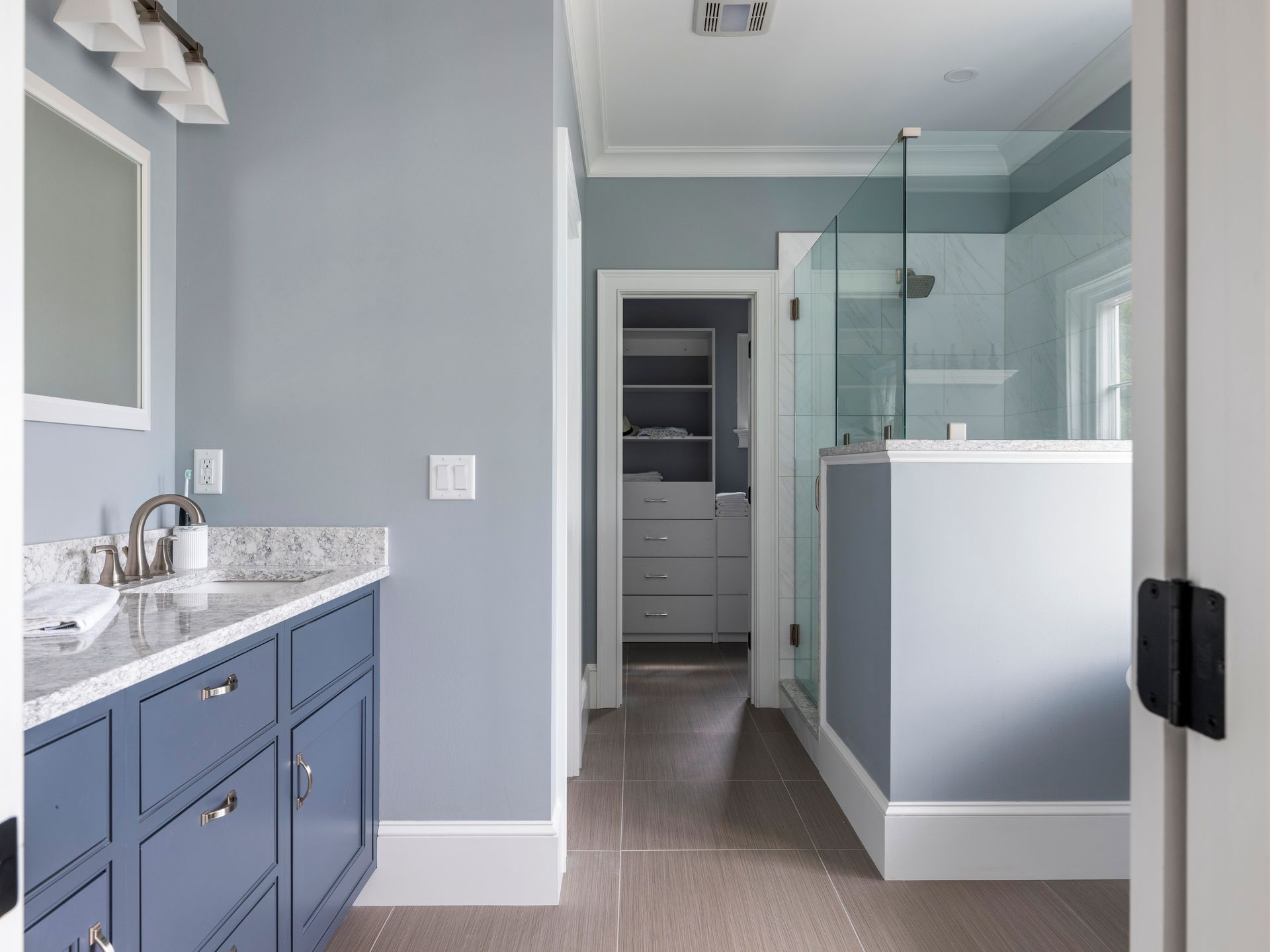Bathroom with blue vanity, granite countertop, glass shower, and gray walls.