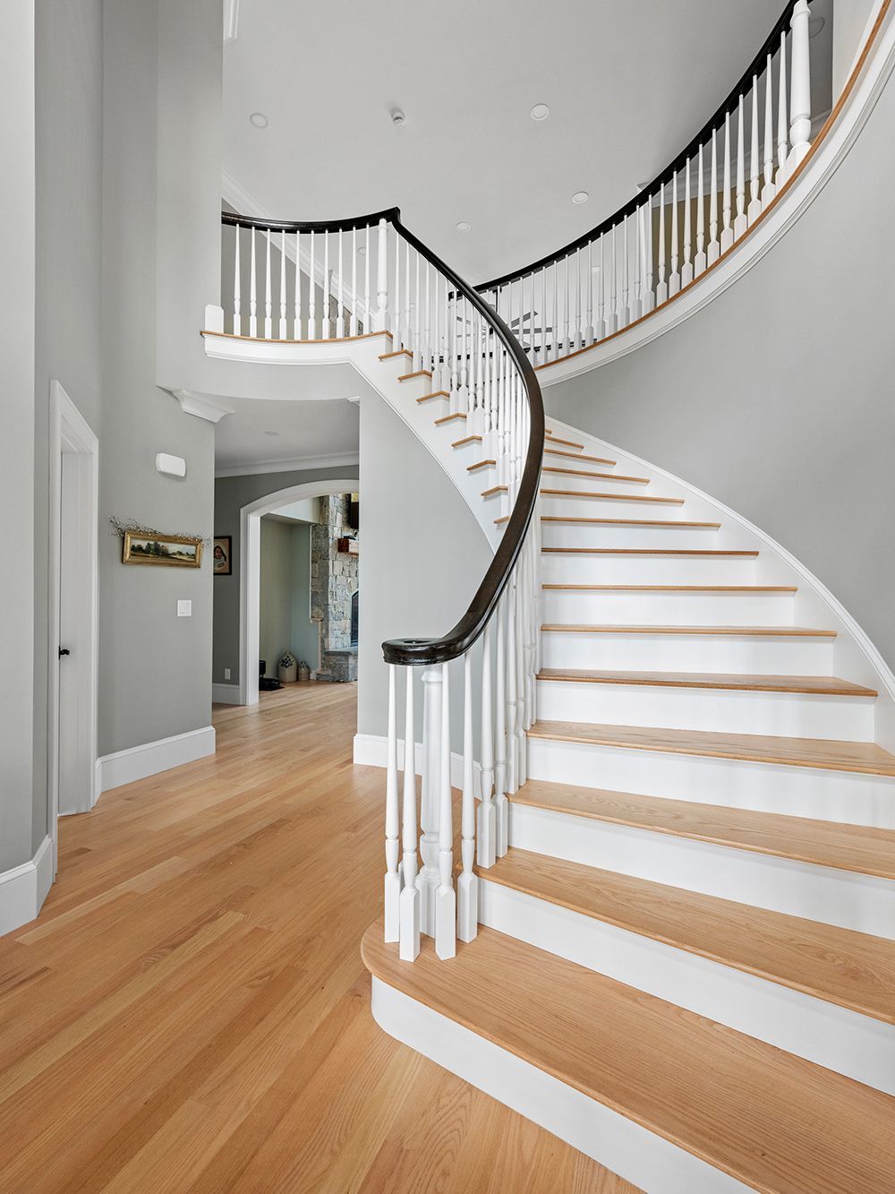 Curved wooden staircase with white balusters, dark handrail, and light wood floors in a gray-walled entryway.