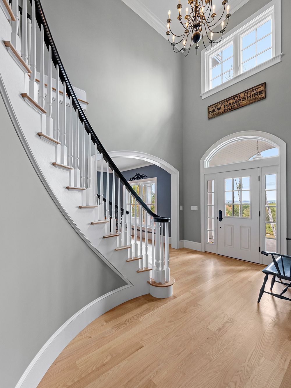 Elegant entryway with curved staircase, hardwood floor, chandelier, and double front doors.