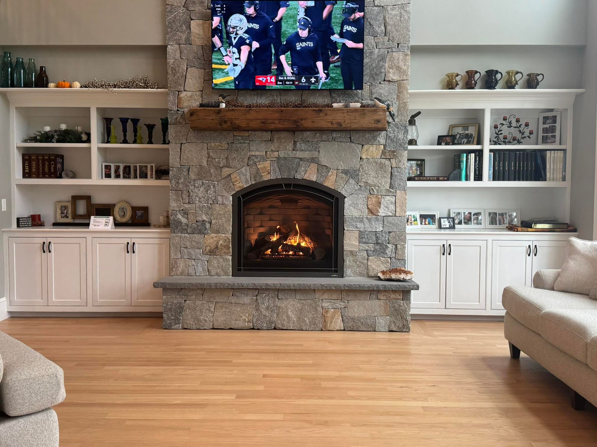 Fireplace with stone surround, TV, built-in shelves, and hardwood floor.