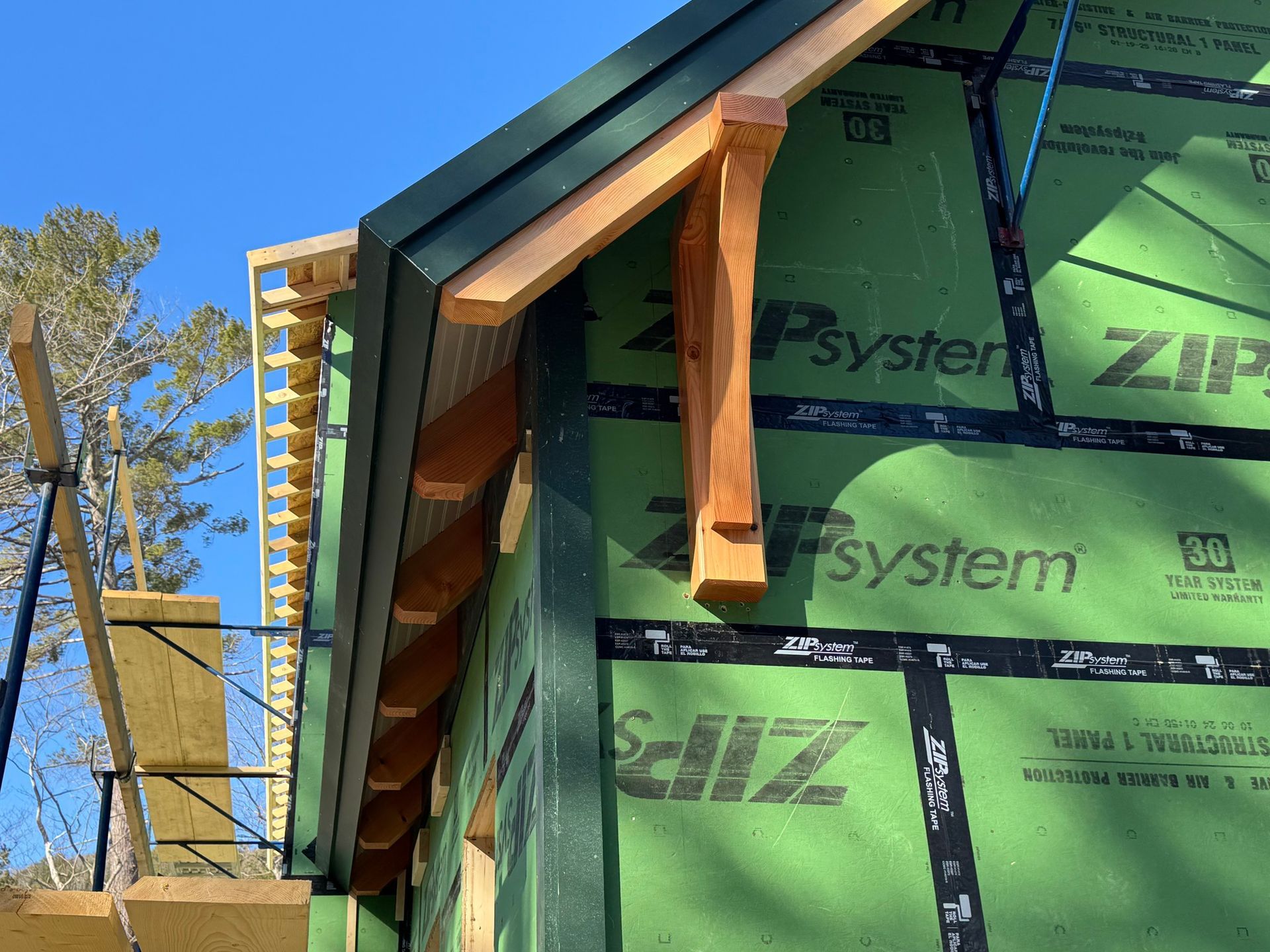 Partially built house exterior with green siding, wooden trim, and blue sky.