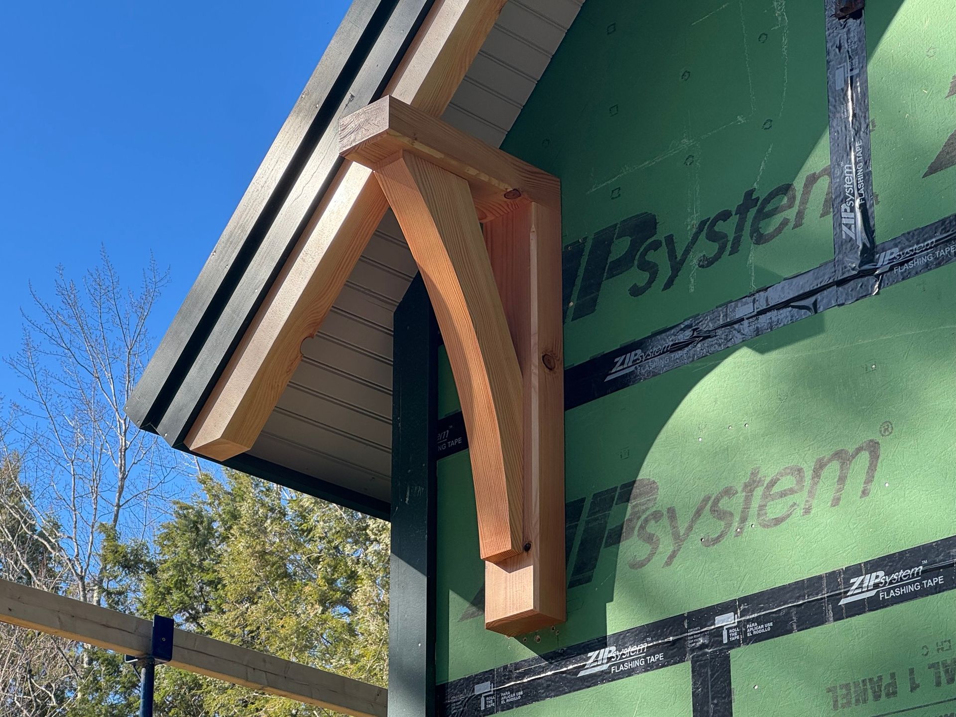 Wooden corbel supporting a roof overhang on a building with green siding and black trim.