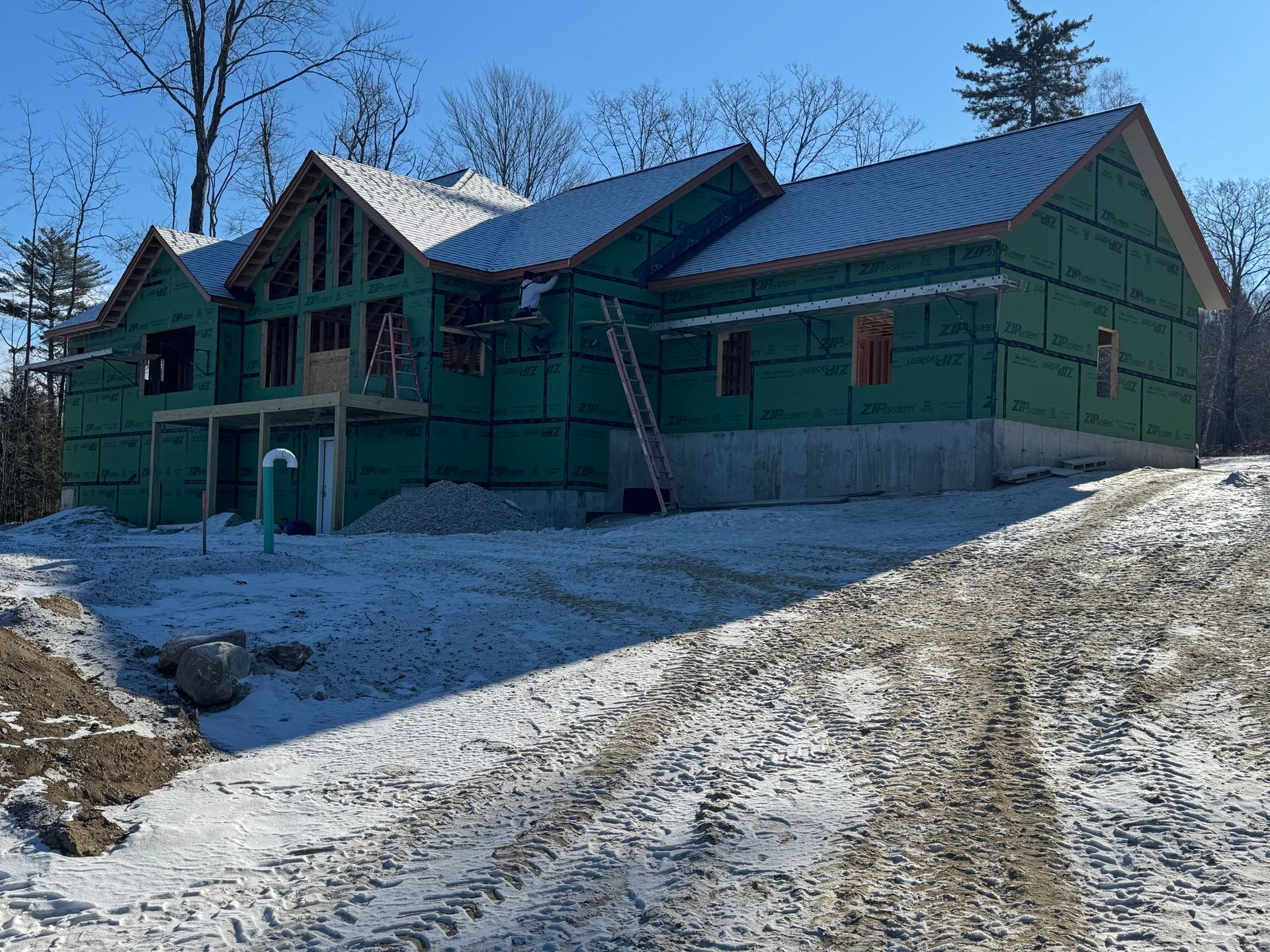 Construction site of a house, covered in green sheeting, with snowy ground.