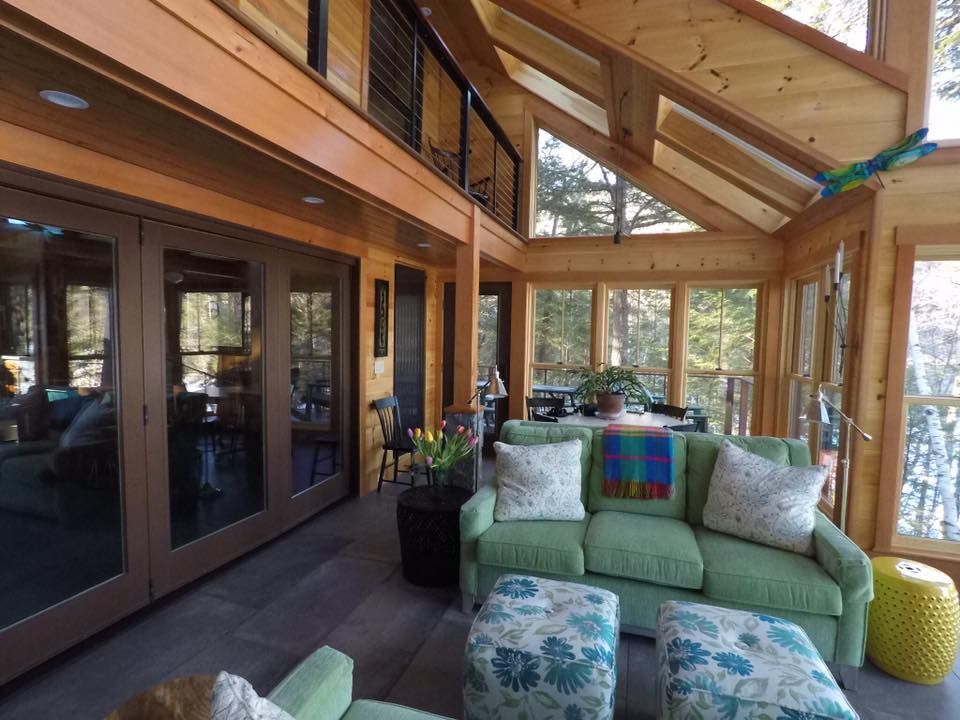 Bright sunroom with wood beams, glass doors, and a green couch with patterned pillows.