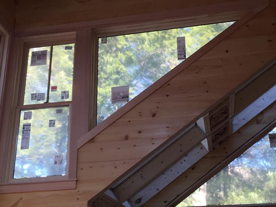 Interior view of a wooden window and a sloped, wood-paneled wall with visible framing; outdoors seen through windows.