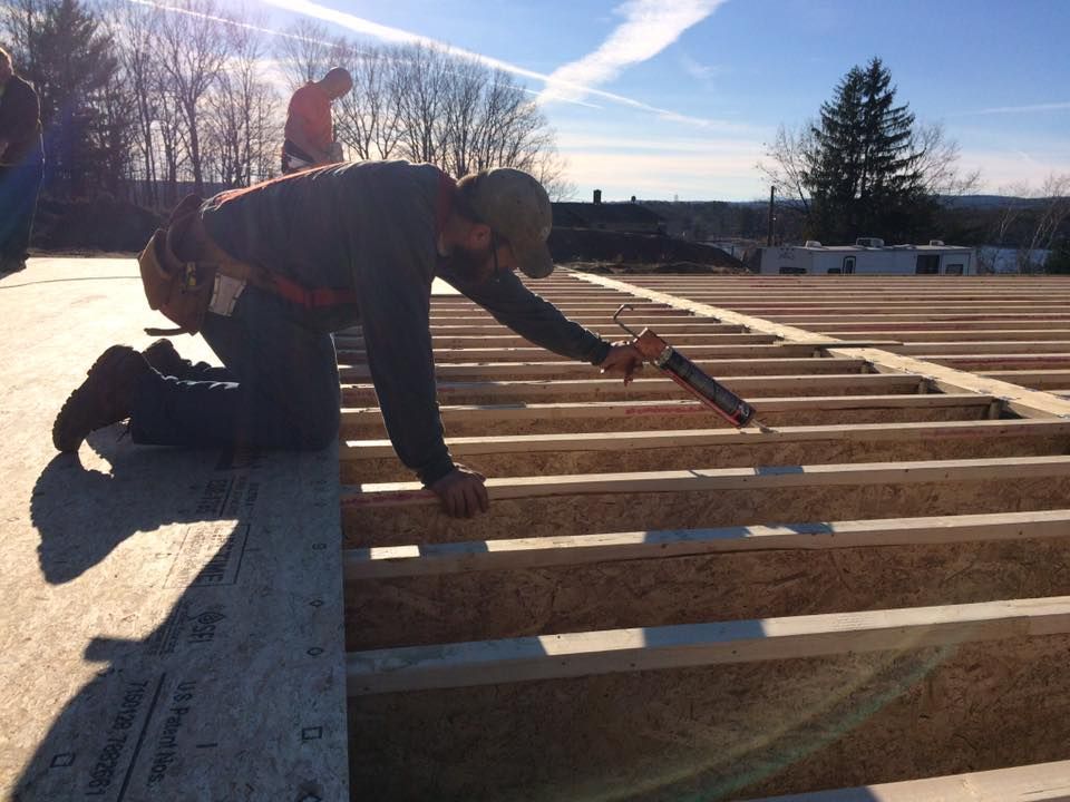 Construction worker kneeling, applying sealant to floor joists on a sunny day.