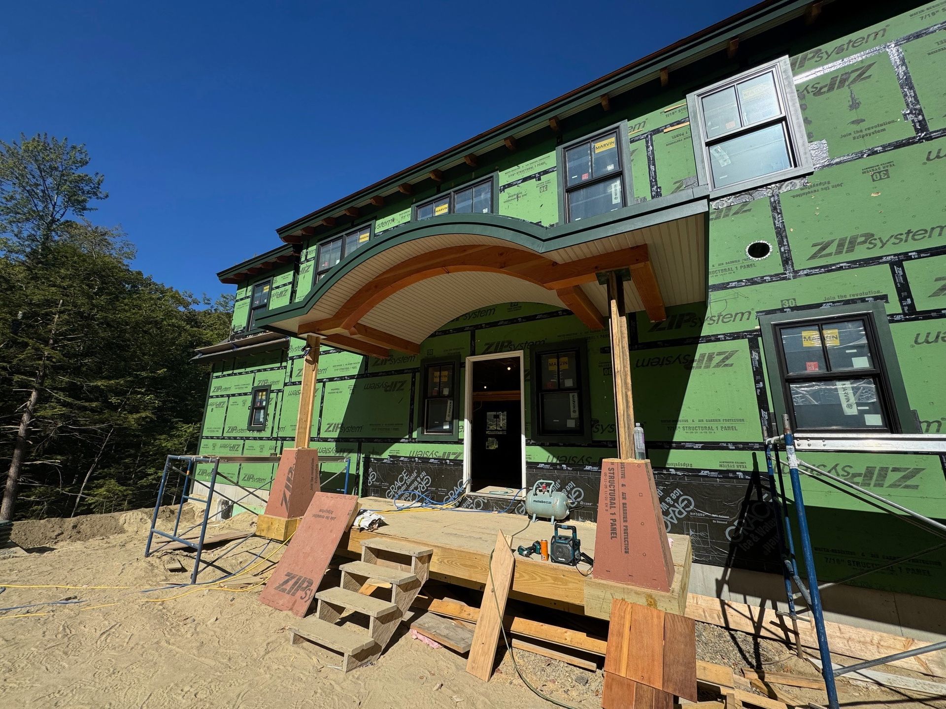 House under construction, green sheathing, curved porch roof, wooden supports, steps.