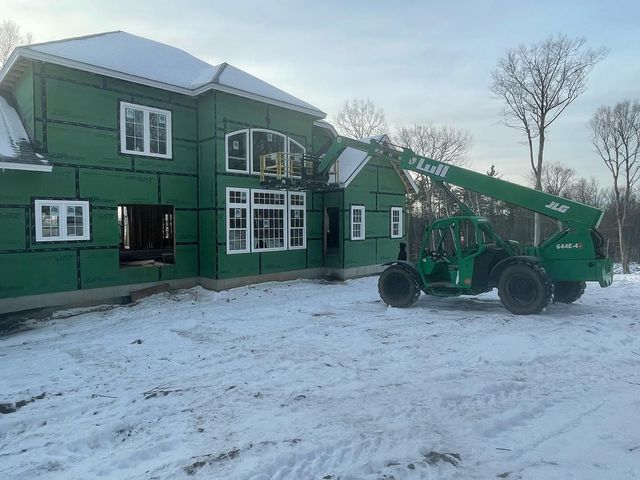 A green building under construction in a snowy landscape; a green telehandler is working on the building.