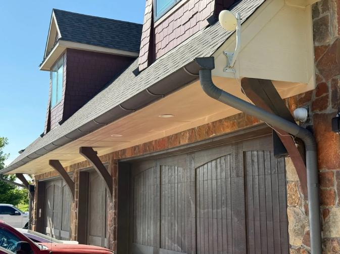 Garage exterior with brown wooden doors, stone walls, gray gutters, and a red car in the foreground.