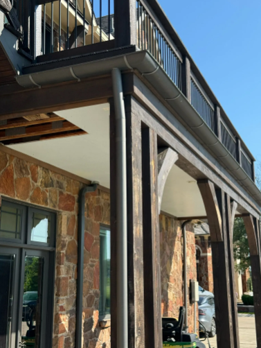 Brown wooden building with stone walls, metal gutters, and second-floor balcony.